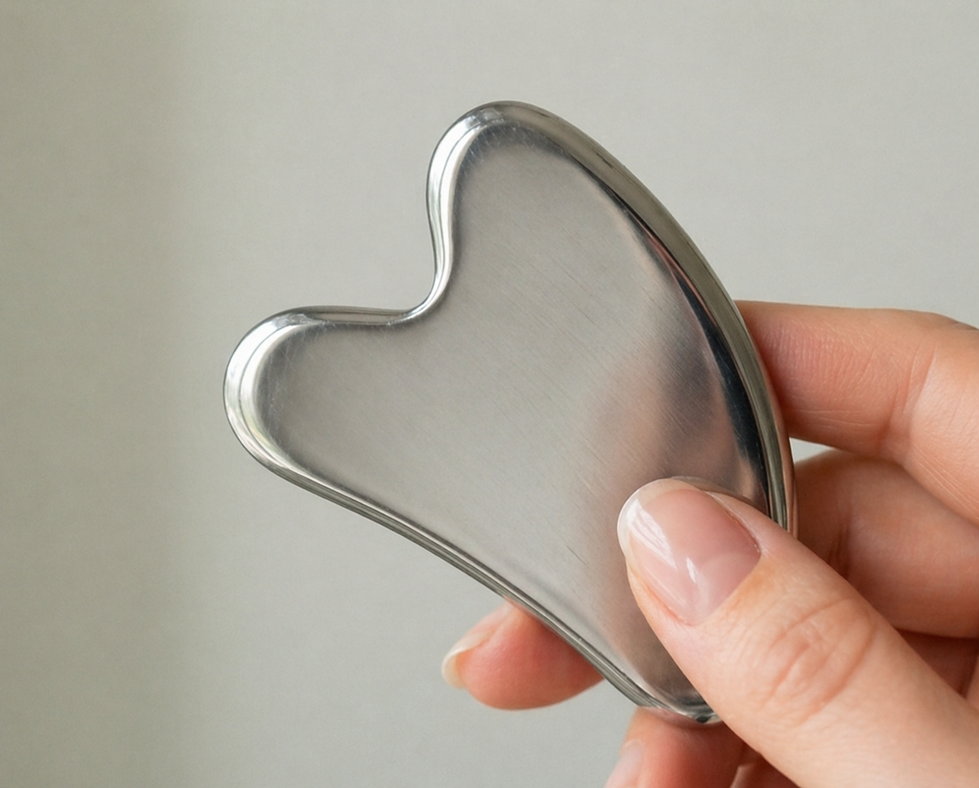 Close-up of the Luminae stainless steel gua sha held between fingertips